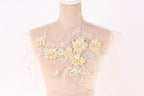 A mannequin with a sheer, lace-like fabric on its back, adorned with delicate yellow flowers and leaves.