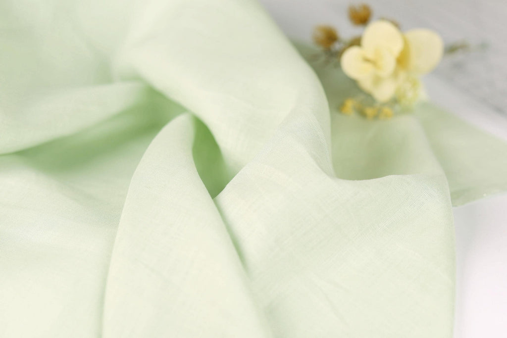 A close-up view of a light green fabric, possibly a piece of linen or a similar material, with a small yellow flower resting on top of it.
