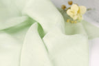 A close-up view of a light green fabric, possibly a piece of linen or a similar material, with a small yellow flower resting on top of it.