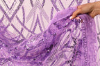 A hand is holding a piece of purple fabric with sequin patterns, which appears to be a decorative textile or garment.