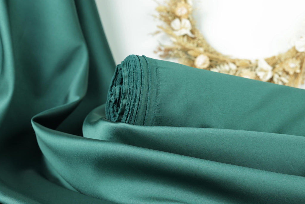 A close-up view of a green satin fabric, with a wreath of dried flowers visible in the background.