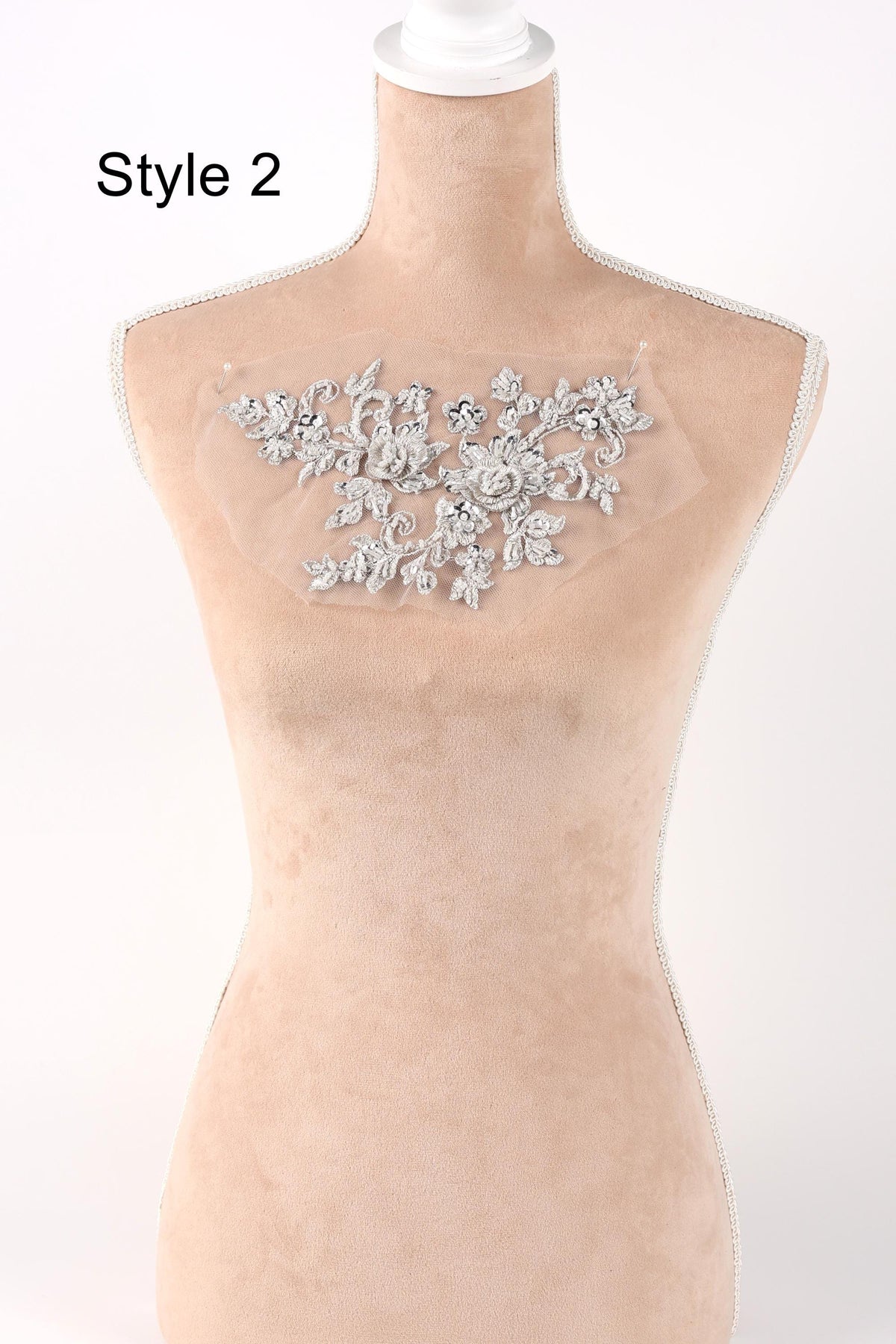 A mannequin with a beige body and a white head, wearing a white lace or floral embroidery on the bust area.