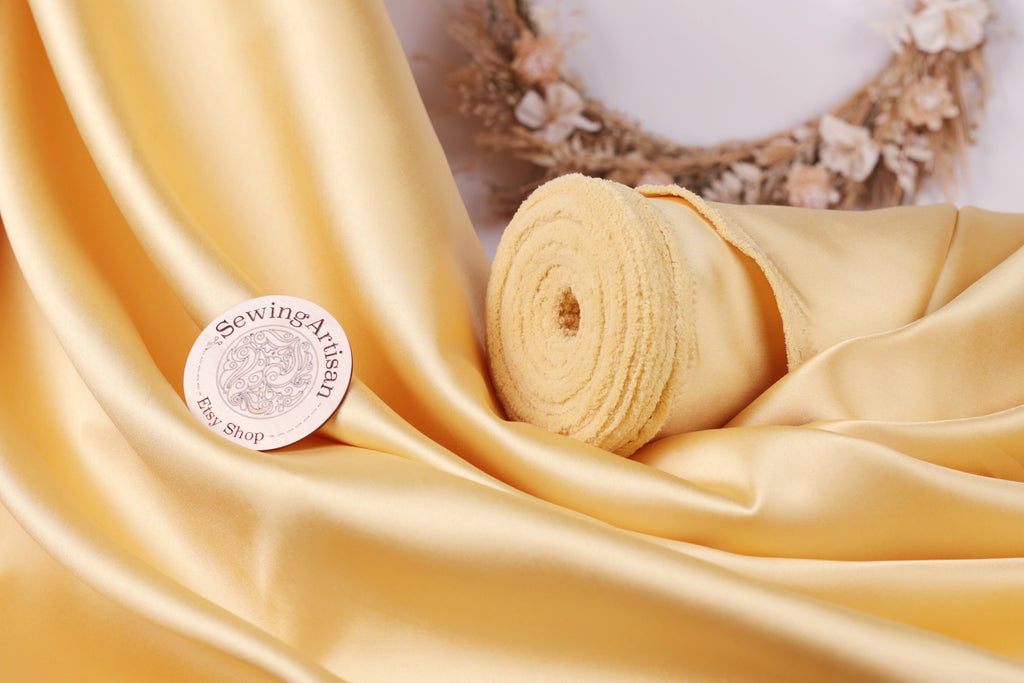 a yellow fabric with a sewing machine logo, a rolled-up piece of fabric, and a wreath with flowers in the background.