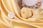 a yellow fabric with a sewing machine logo, a rolled-up piece of fabric, and a wreath with flowers in the background.