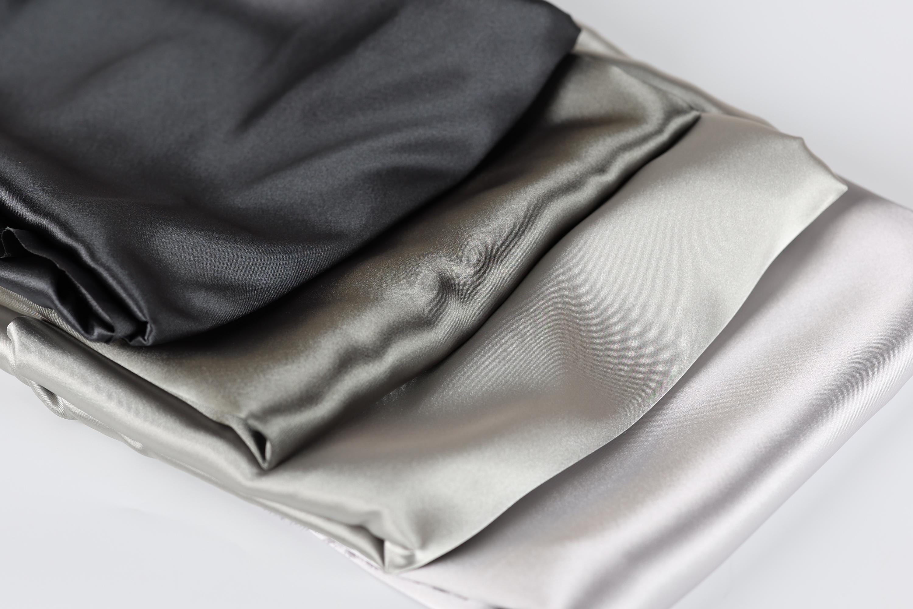a close-up view of three different colored satin fabrics, including black, gray, and white, arranged in a layered fashion.