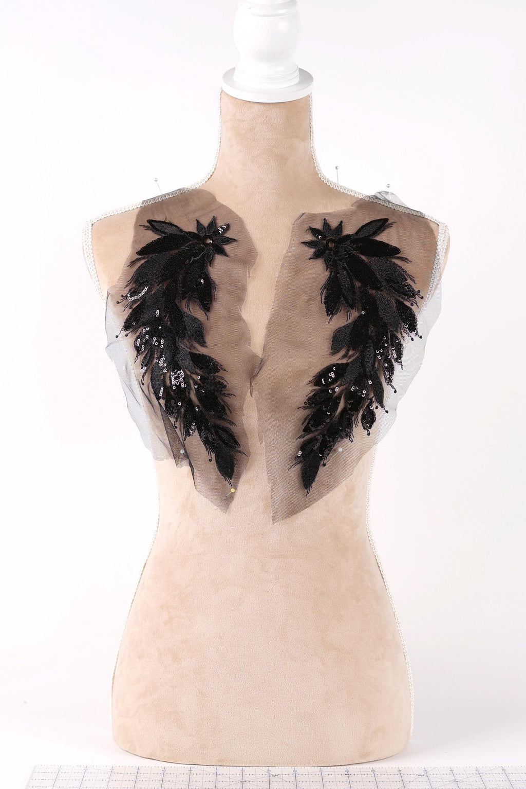 A mannequin with a beige body and a white head, wearing a dress with black feather embellishments on the shoulders.