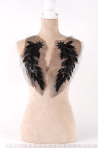 A mannequin with a beige body and a white head, wearing a dress with black feather embellishments on the shoulders.