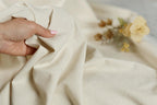 A hand is holding a piece of white fabric, with a blurred background featuring a bouquet of yellow flowers.