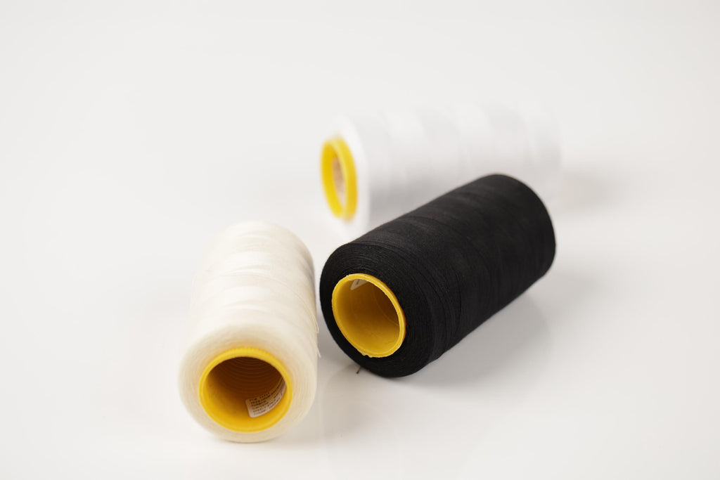Three spools of thread in different colors - white, black, and yellow - are arranged on a white background.