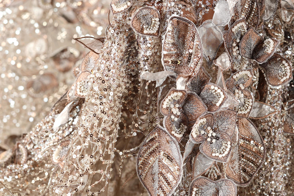 The image is a close-up of a fabric with intricate gold and silver embroidery, including flowers and leaves. The fabric appears to be a decorative piece, possibly used for clothing or other textile applications.