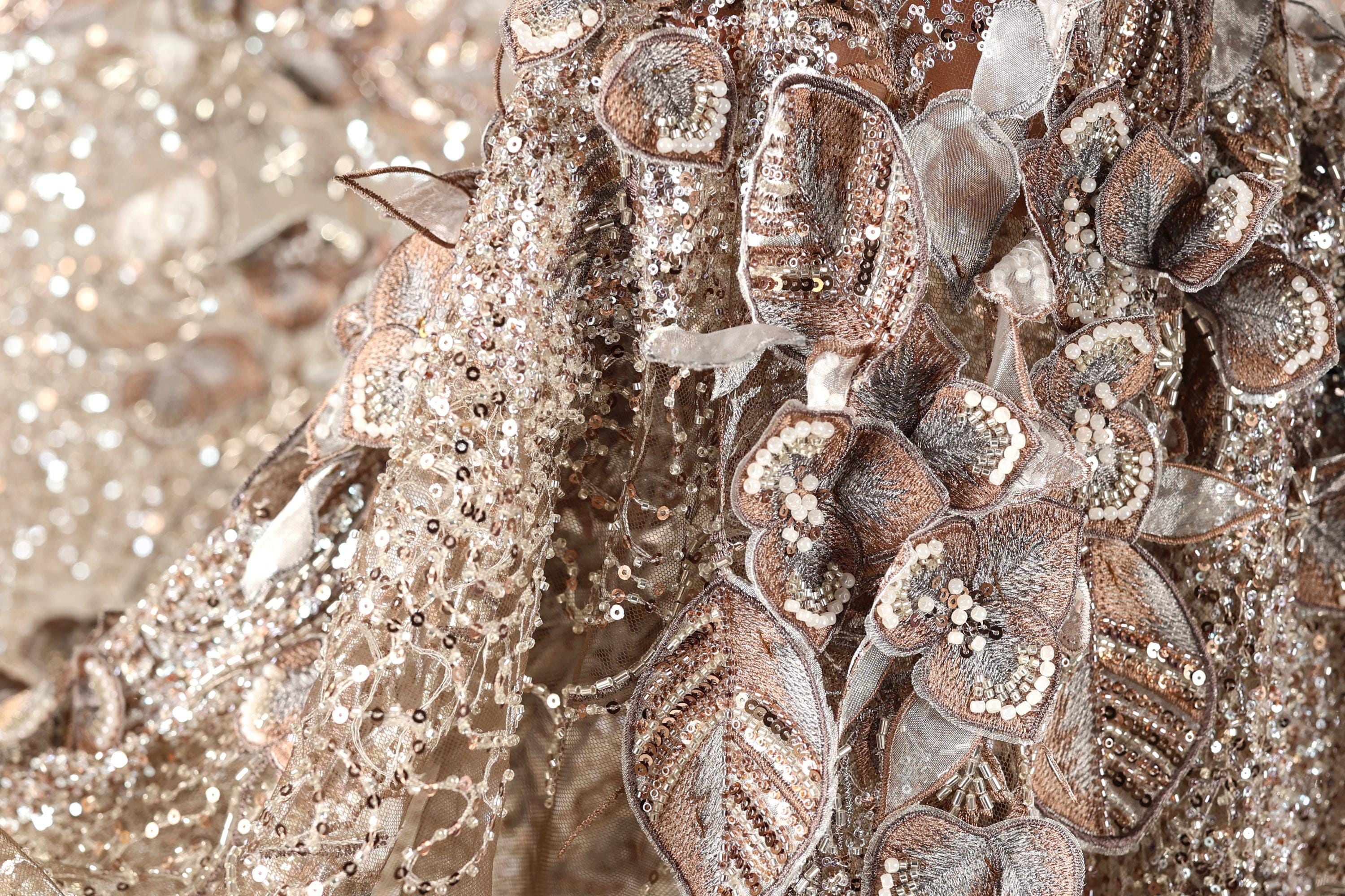 The image is a close-up of a fabric with intricate gold and silver embroidery, including flowers and leaves. The fabric appears to be a decorative piece, possibly used for clothing or other textile applications.