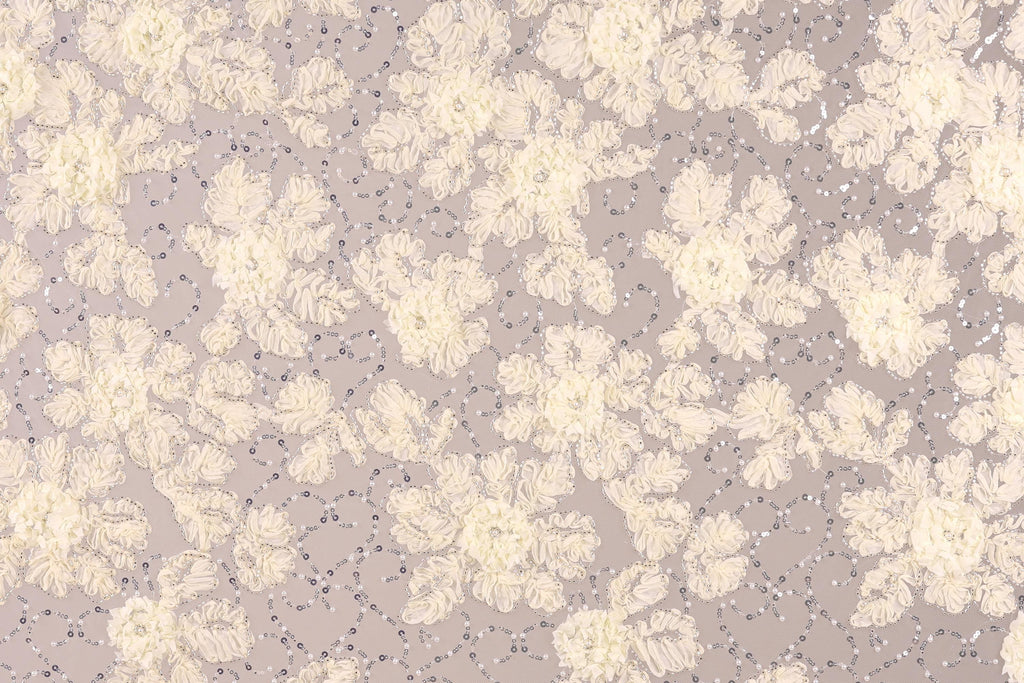 a close-up view of a fabric with a floral pattern, including white and beige flowers and small silver sequins or beads scattered throughout the fabric.