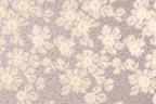 a close-up view of a fabric with a floral pattern, including white and beige flowers and small silver sequins or beads scattered throughout the fabric.