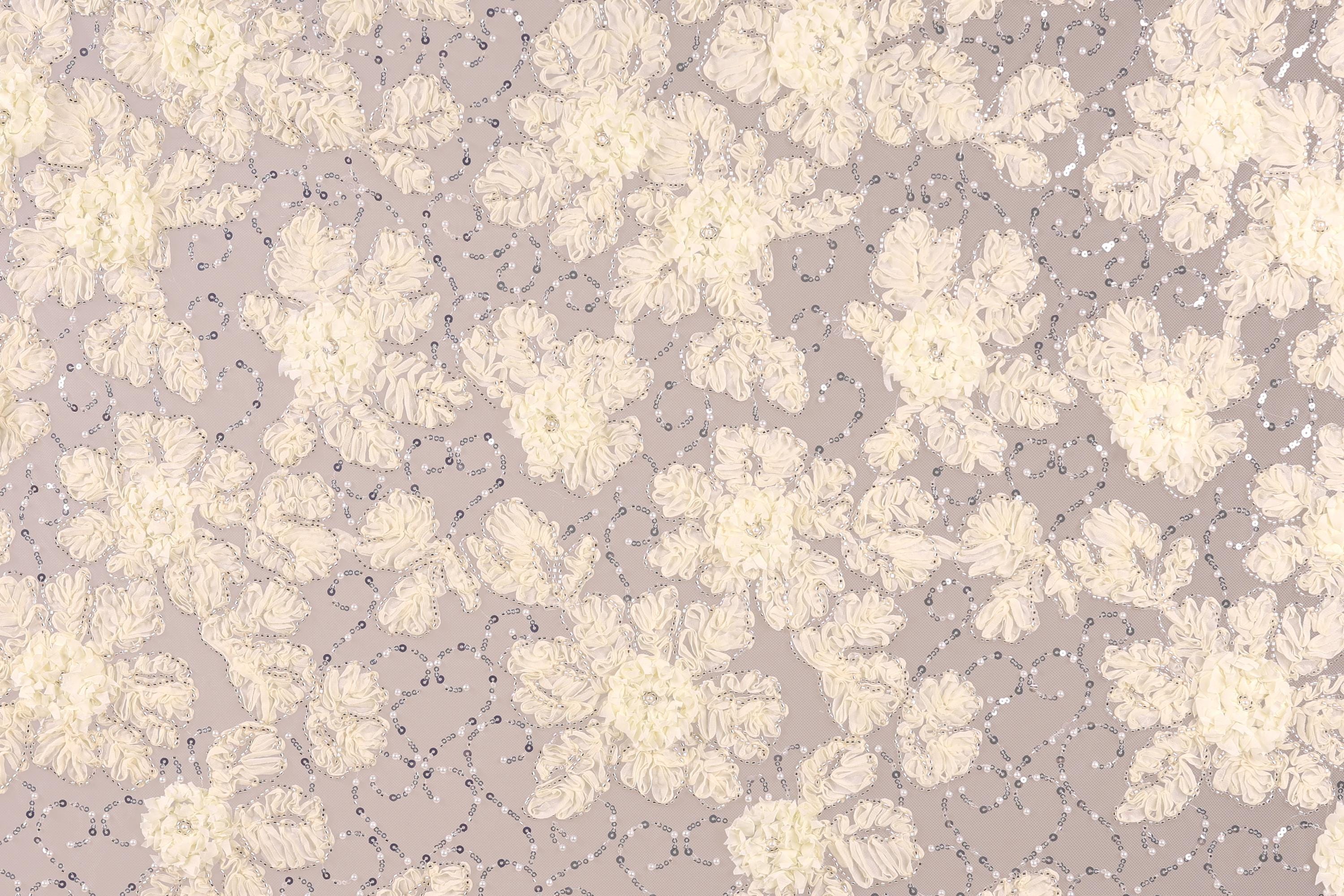 a close-up view of a fabric with a floral pattern, including white and beige flowers and small silver sequins or beads scattered throughout the fabric.