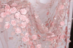 a close-up view of a delicate, pink floral fabric with numerous small, intricately designed roses and leaves. The fabric appears to be made of sheer material, giving it a soft and delicate appearance. The roses and leaves are arranged in a way that creates a visually appealing and intricate pattern, showcasing the craftsmanship and attention to detail in the fabric.