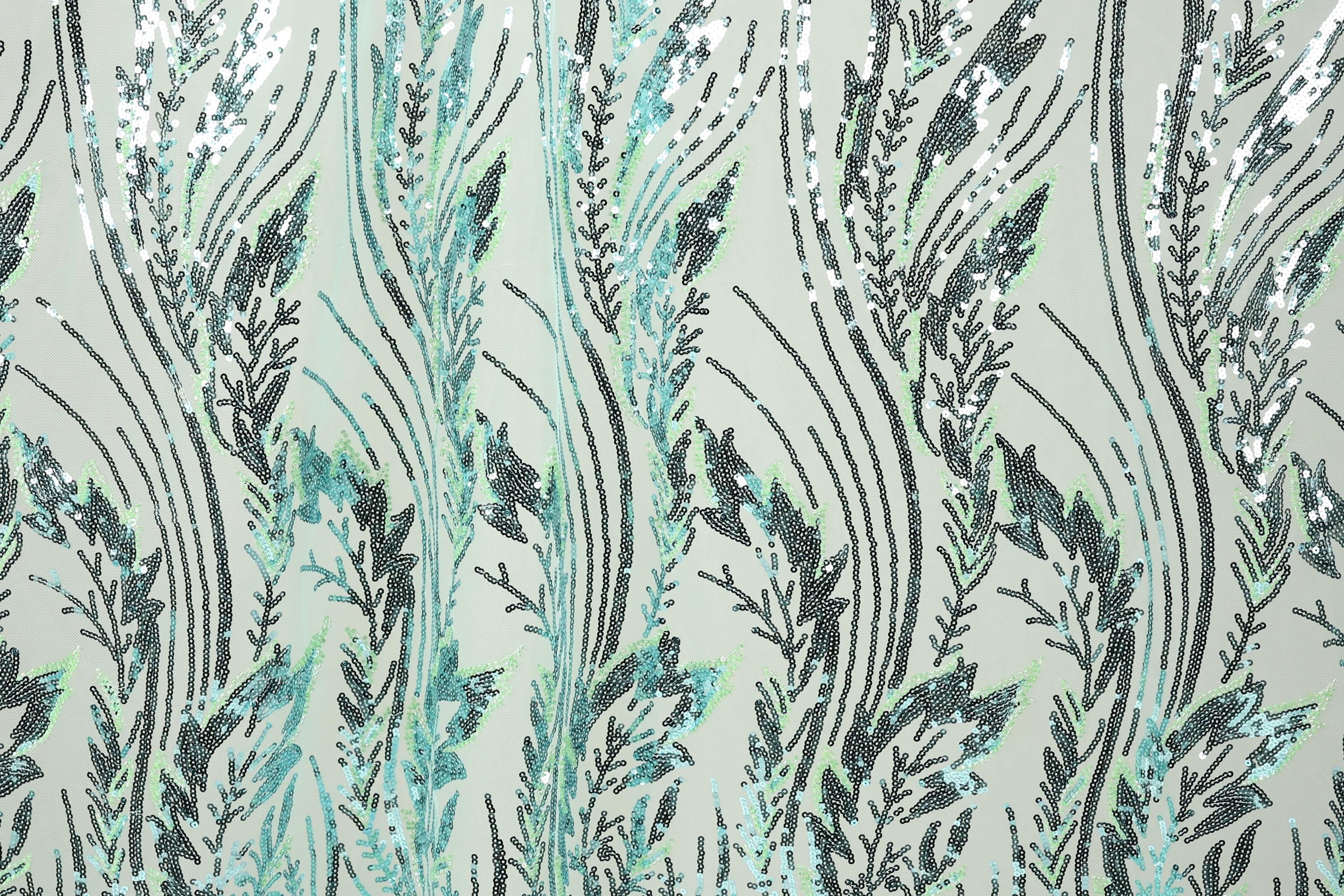a close-up view of a fabric with a repeating pattern of green and black sequin designs. The pattern consists of various lines and shapes, creating a visually striking and intricate design. The fabric appears to be a light green color, which contrasts with the dark green and black sequin elements. The image does not contain any text or other discernible objects, and the focus is solely on the detailed pattern of the fabric.