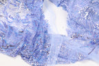 a close-up view of a fabric with a blue and silver sequined pattern. The fabric appears to be a sheer material, with a delicate and intricate design. The background is white, which contrasts with the vibrant colors of the sequins and fabric. The image does not contain any text or other discernible objects, and the focus is solely on the fabric and its details.