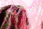 A close-up view of a vibrant, intricately embroidered fabric with a pink and green color scheme.