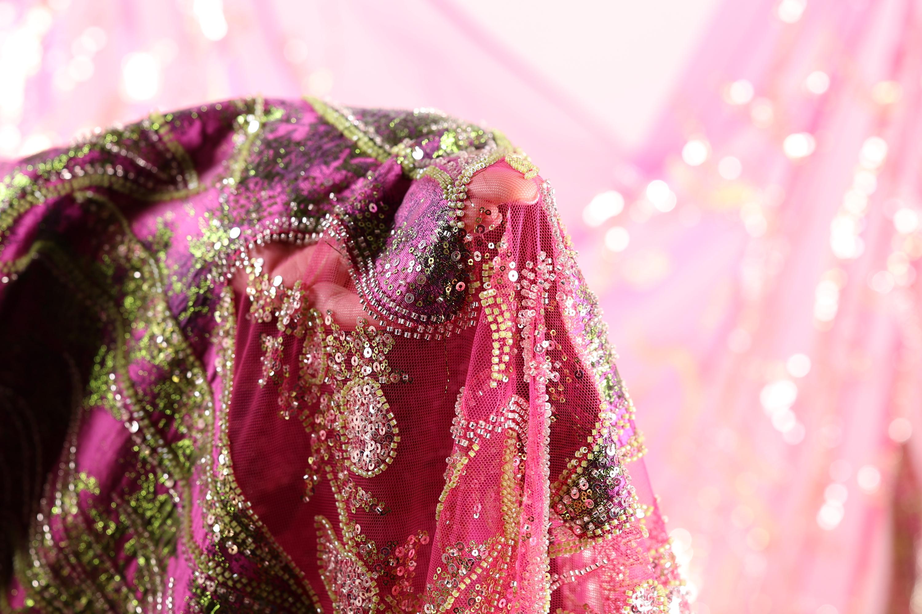 A close-up view of a vibrant, intricately embroidered fabric with a pink and green color scheme.