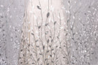 a close-up view of a delicate, white dress with a pattern of silver and white leaves or branches. The dress appears to be made of a sheer fabric, giving it a delicate and elegant appearance.