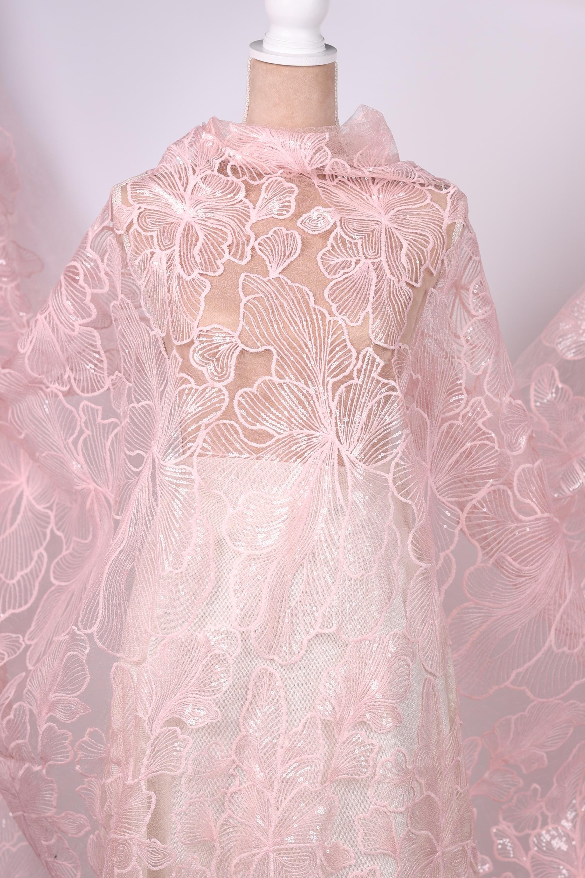 a close-up view of a delicate, pink lace fabric with a floral pattern. The fabric appears to be made of sheer material, giving it a soft and delicate appearance.