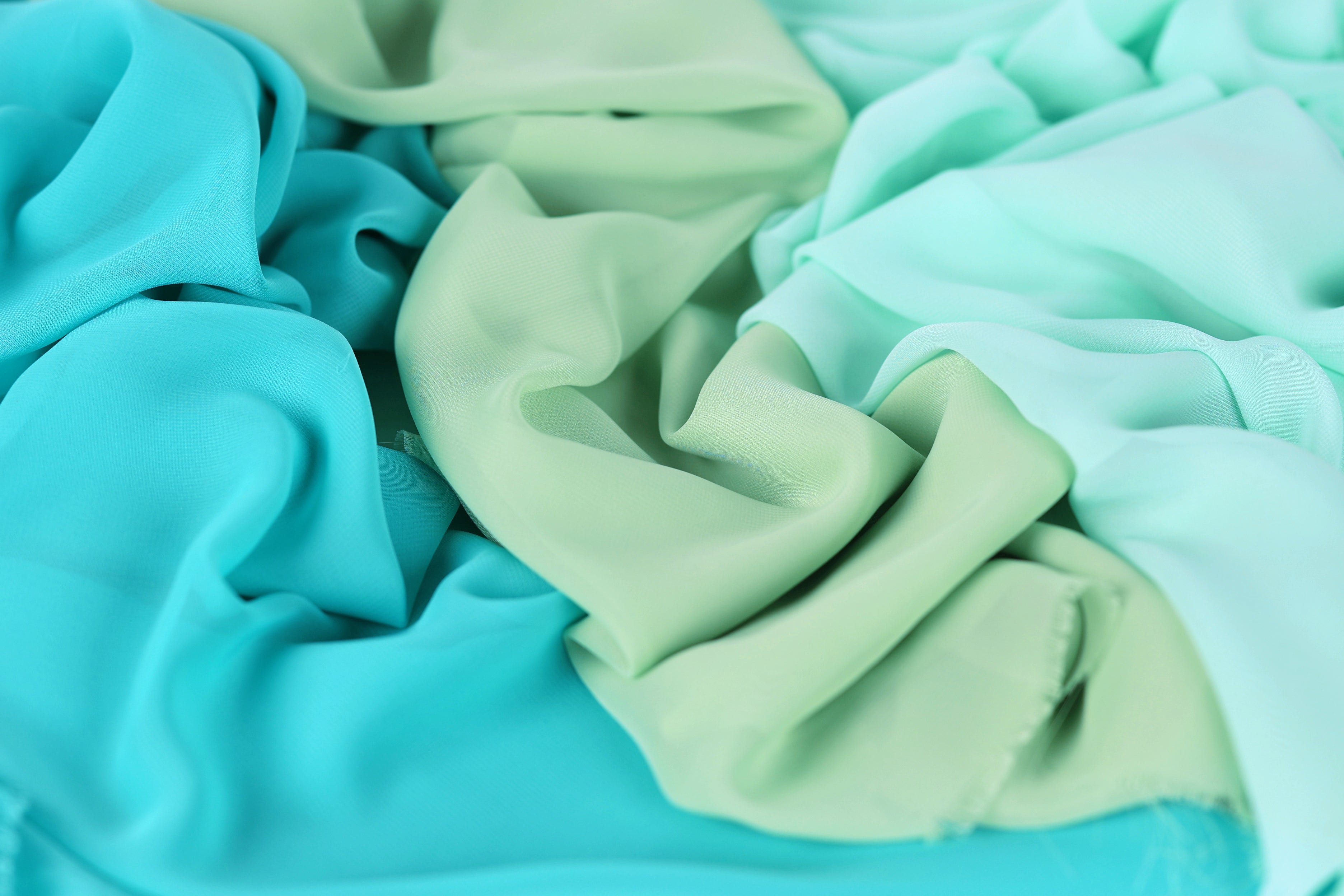 a close-up view of a pile of fabric with a mix of turquoise and mint green colors. The fabric appears to be crumpled and wrinkled, giving it a textured and soft appearance.