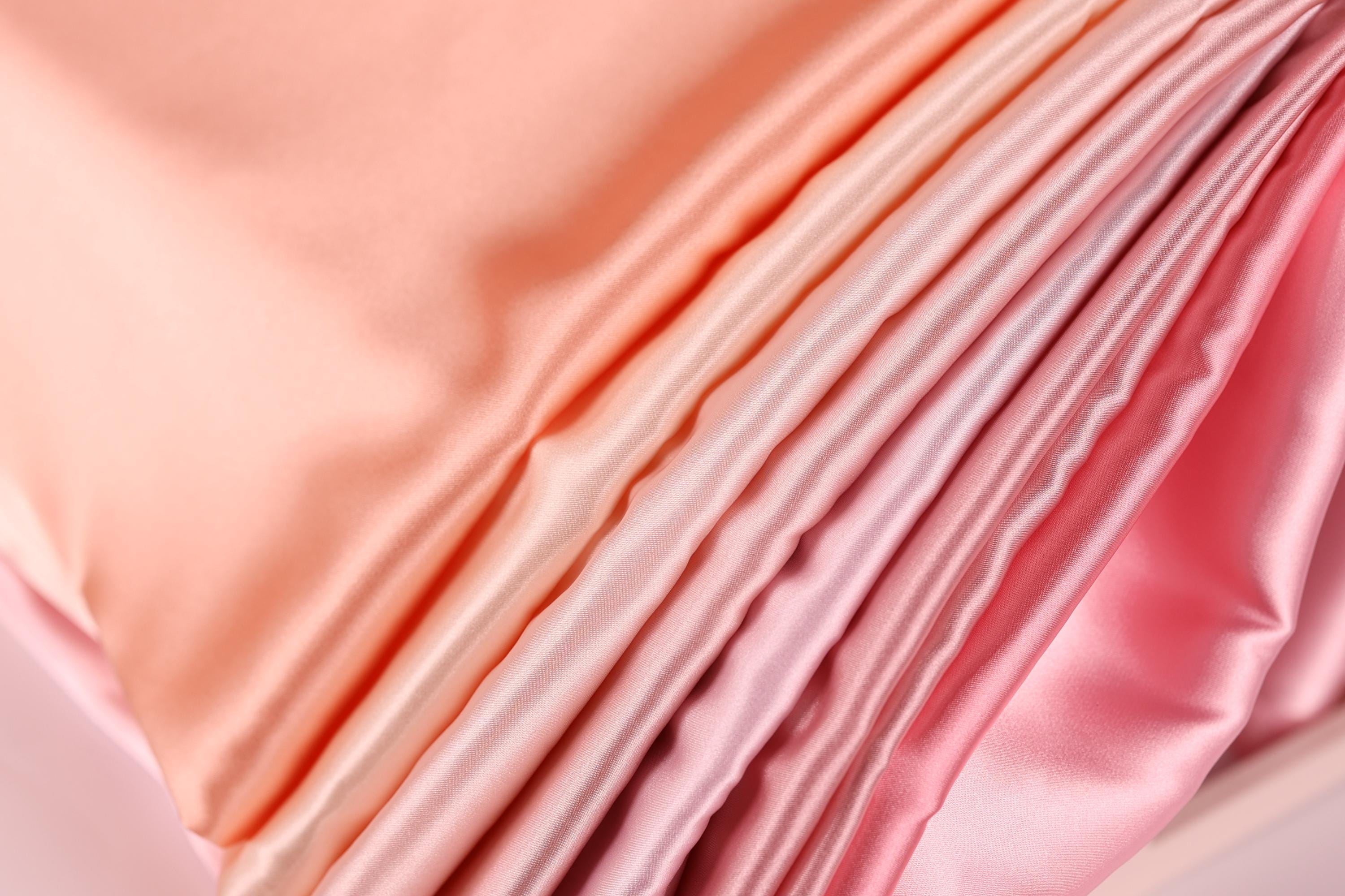 A close-up view of a soft, flowing fabric with a gradient of pink and peach colors, creating a visually appealing and textured appearance.