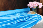a blue satin fabric draped over a table, with a vase of pink peonies placed next to it.