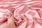 A hand is holding a piece of pink satin fabric, which appears to be soft and smooth.