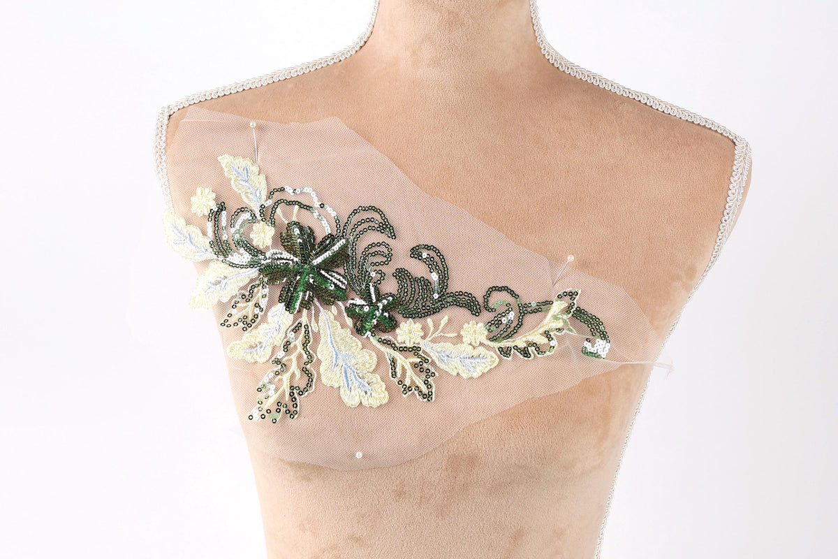A mannequin torso with a decorative green and white floral embroidered piece on it.