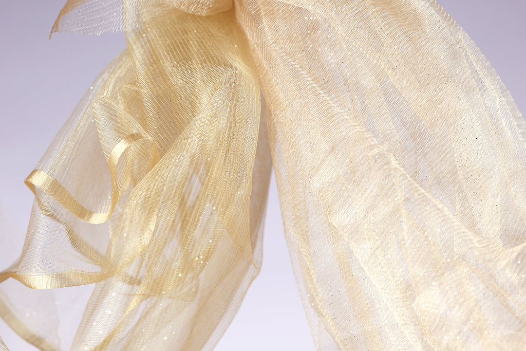 a close-up view of a delicate, shimmering gold fabric, possibly a sheer or sheer-like material, with a soft, flowing texture.