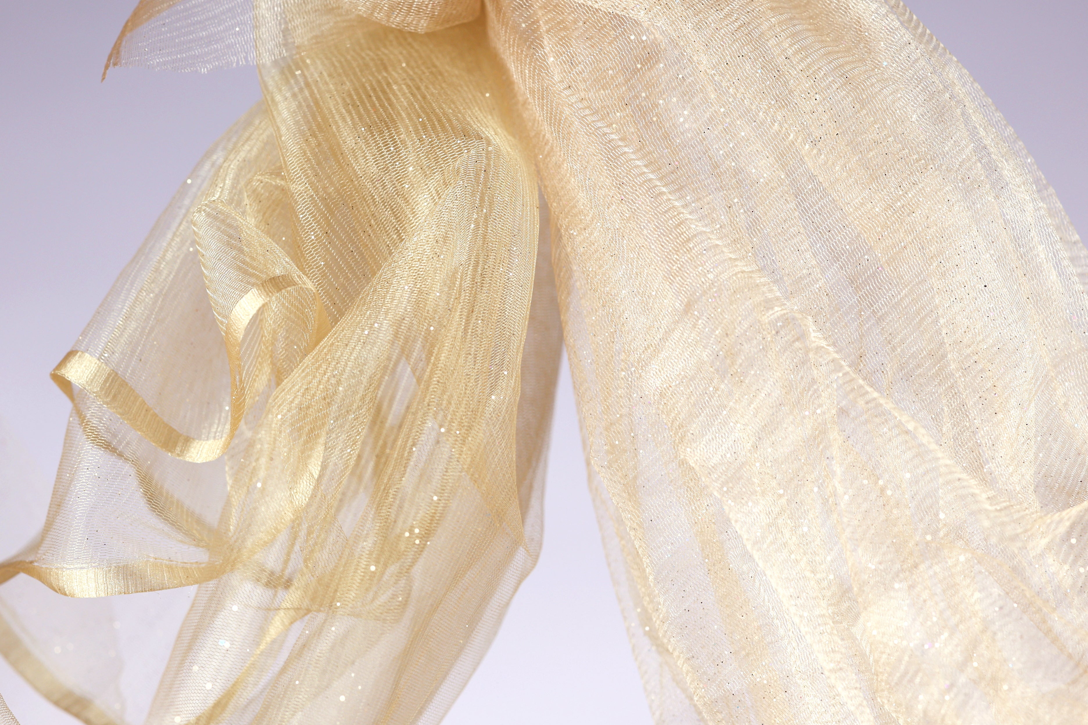 a close-up view of a delicate, shimmering gold fabric, possibly a sheer or sheer-like material, with a soft, flowing texture.