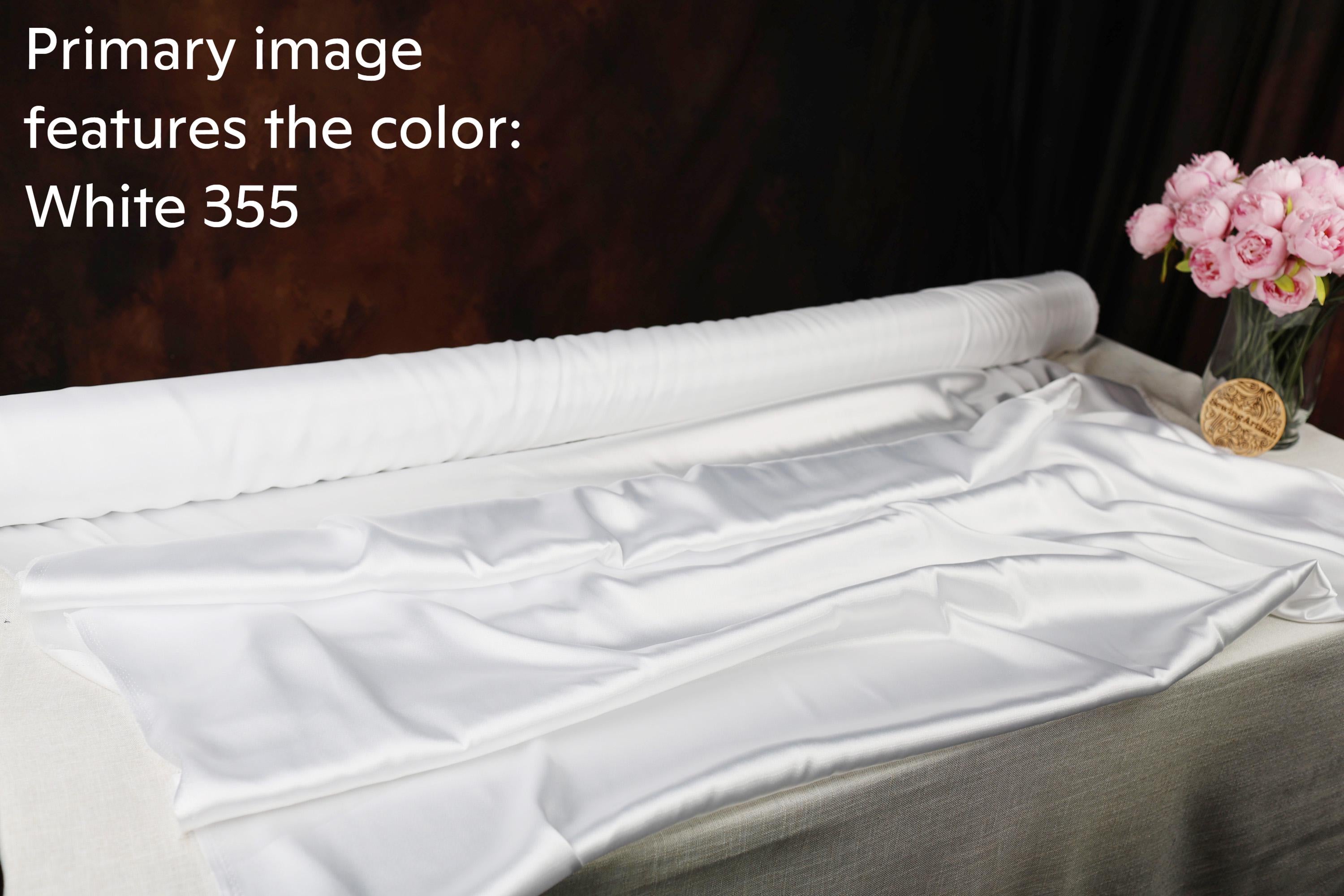 a roll of white fabric with a vase of pink flowers on a table.