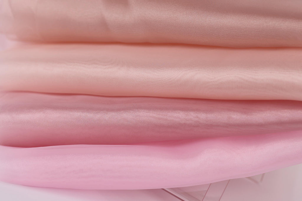 A close-up image of a stack of soft, light pink fabric, with a focus on the texture and color of the fabric.