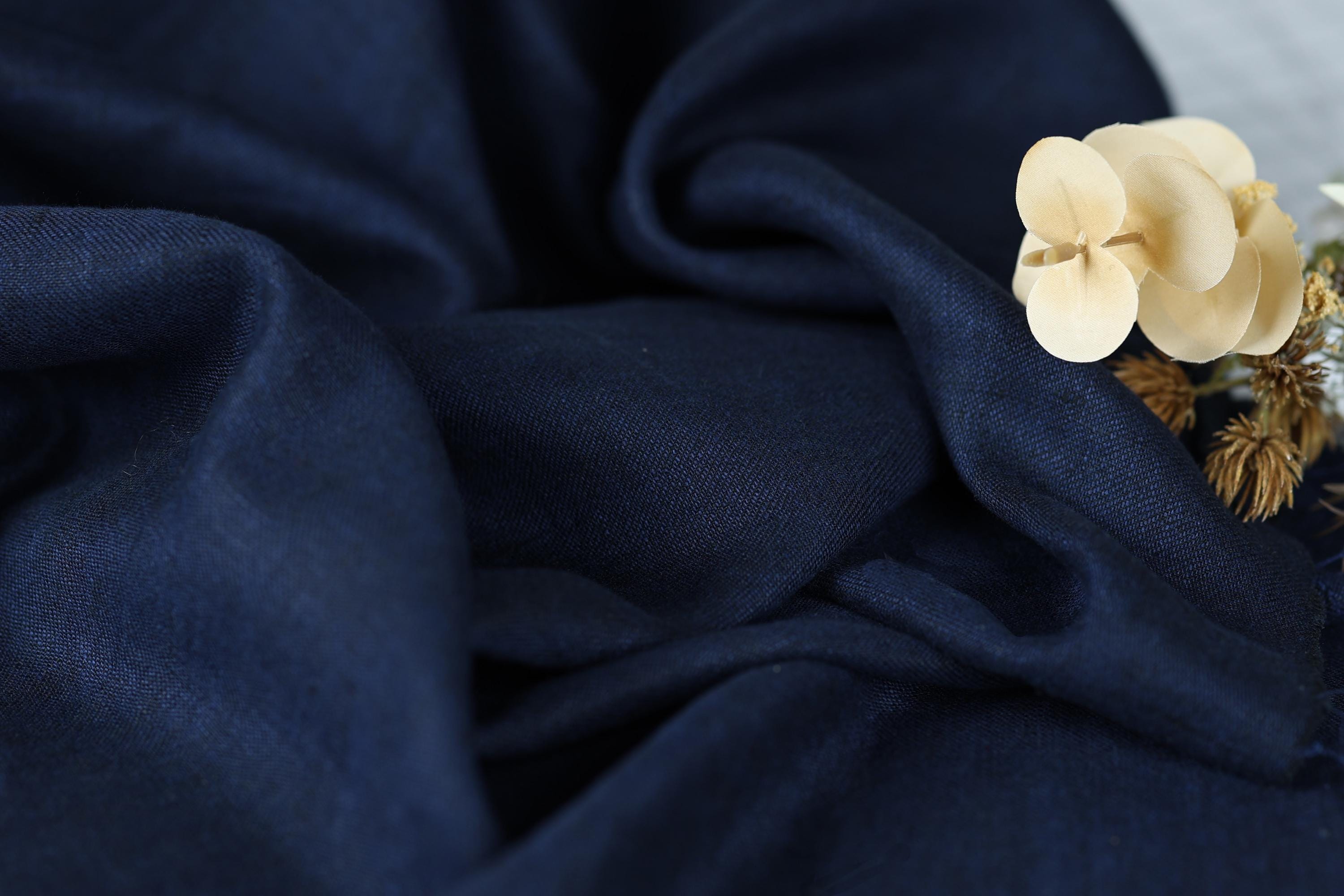 a close-up view of a dark blue fabric with a delicate white flower resting on top of it.