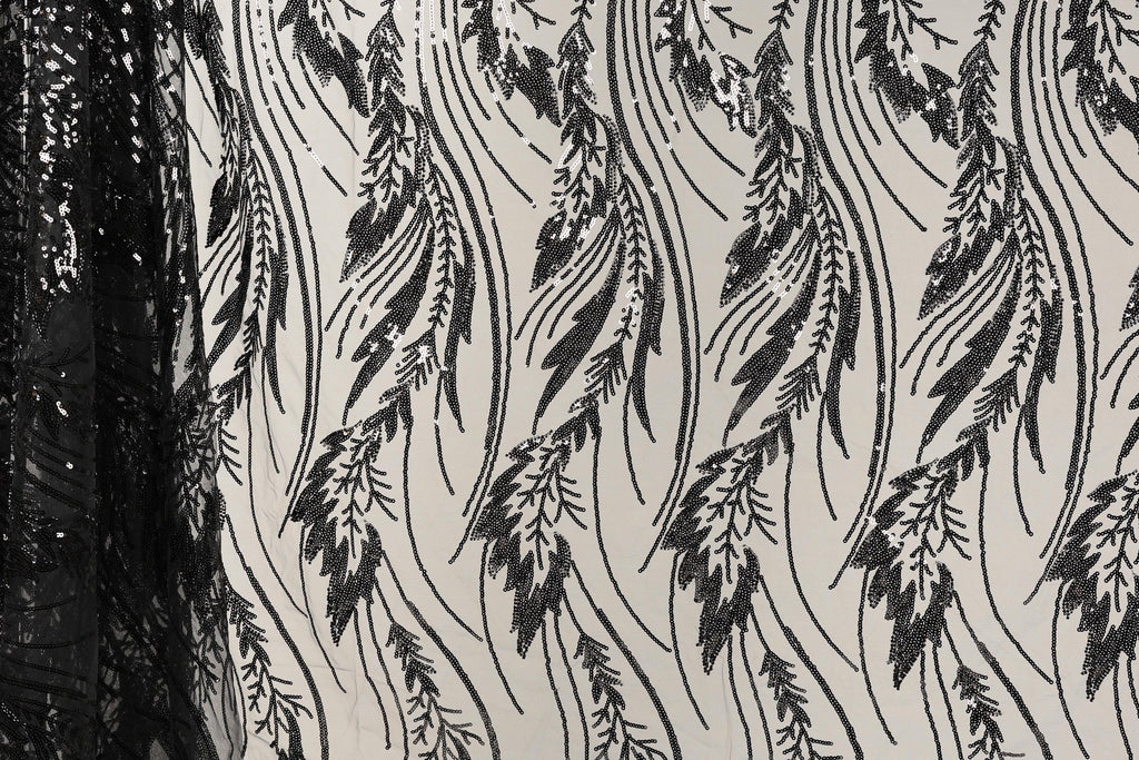 a close-up view of a fabric with a repeating pattern of black and white leaf-like designs. The pattern is intricate and detailed, with the leaves appearing to be made of sequins or beads. The fabric appears to be a sheer material, allowing the leaves to be visible through the sheerness. The image does not contain any text or other discernible objects or actions.