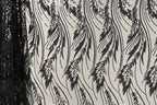 a close-up view of a fabric with a repeating pattern of black and white leaf-like designs. The pattern is intricate and detailed, with the leaves appearing to be made of sequins or beads. The fabric appears to be a sheer material, allowing the leaves to be visible through the sheerness. The image does not contain any text or other discernible objects or actions.