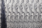 a close-up view of a fabric with a repeating pattern of black and white floral designs. The pattern consists of numerous small leaves and flowers arranged in a repeating diagonal line across the fabric. The fabric appears to be made of a material with a textured surface, which adds depth and visual interest to the overall design.