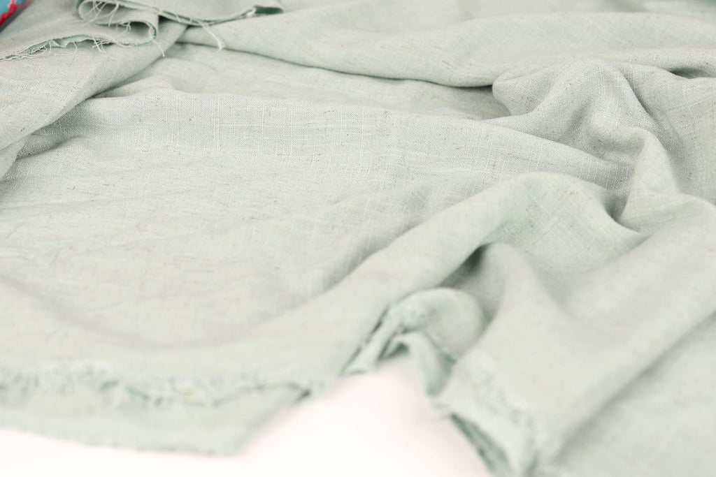 a close-up view of a light green fabric, possibly a piece of clothing or a textile, with visible wrinkles and folds.