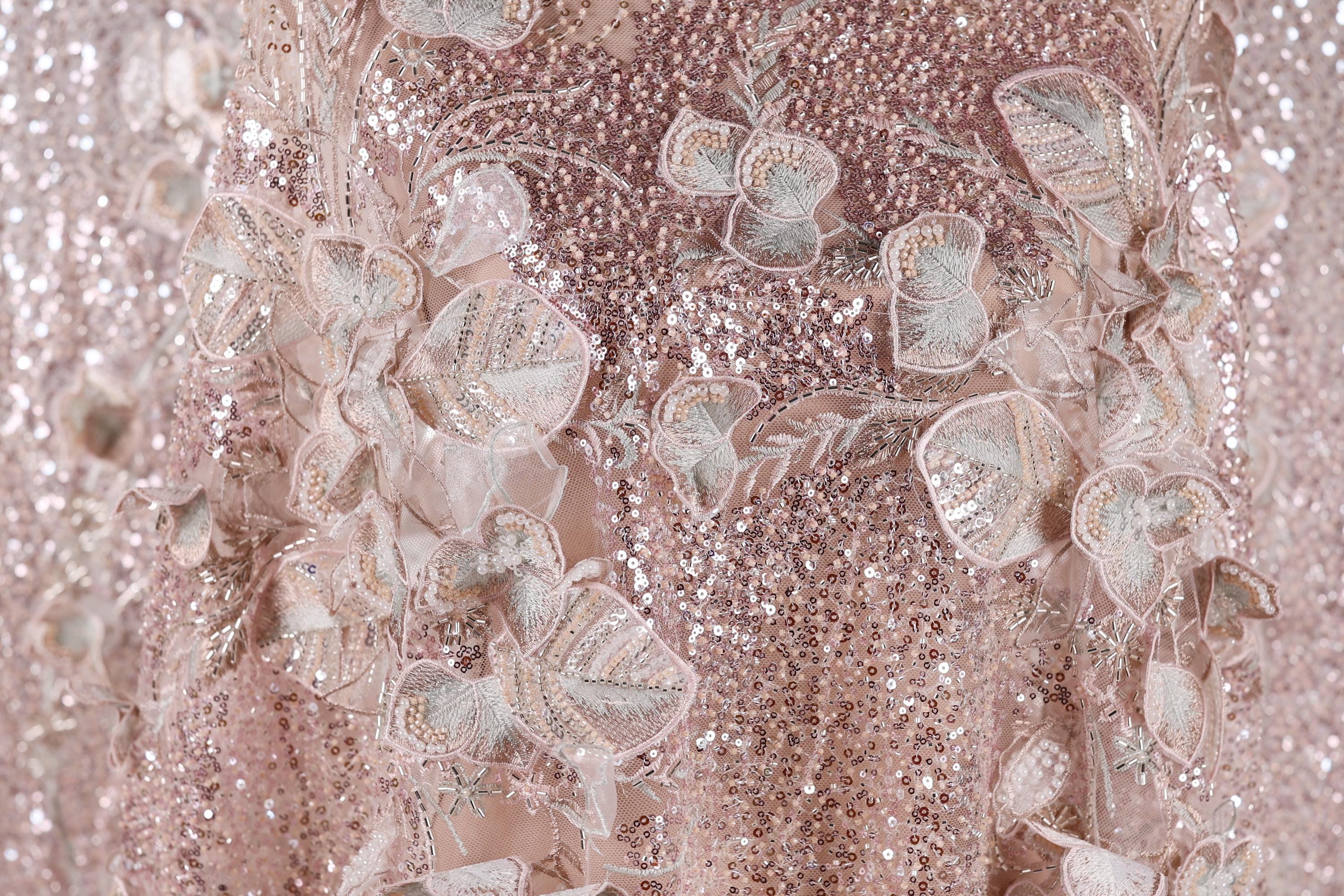 The image is a close-up of a delicate, pink sequined dress with intricate floral embroidery.