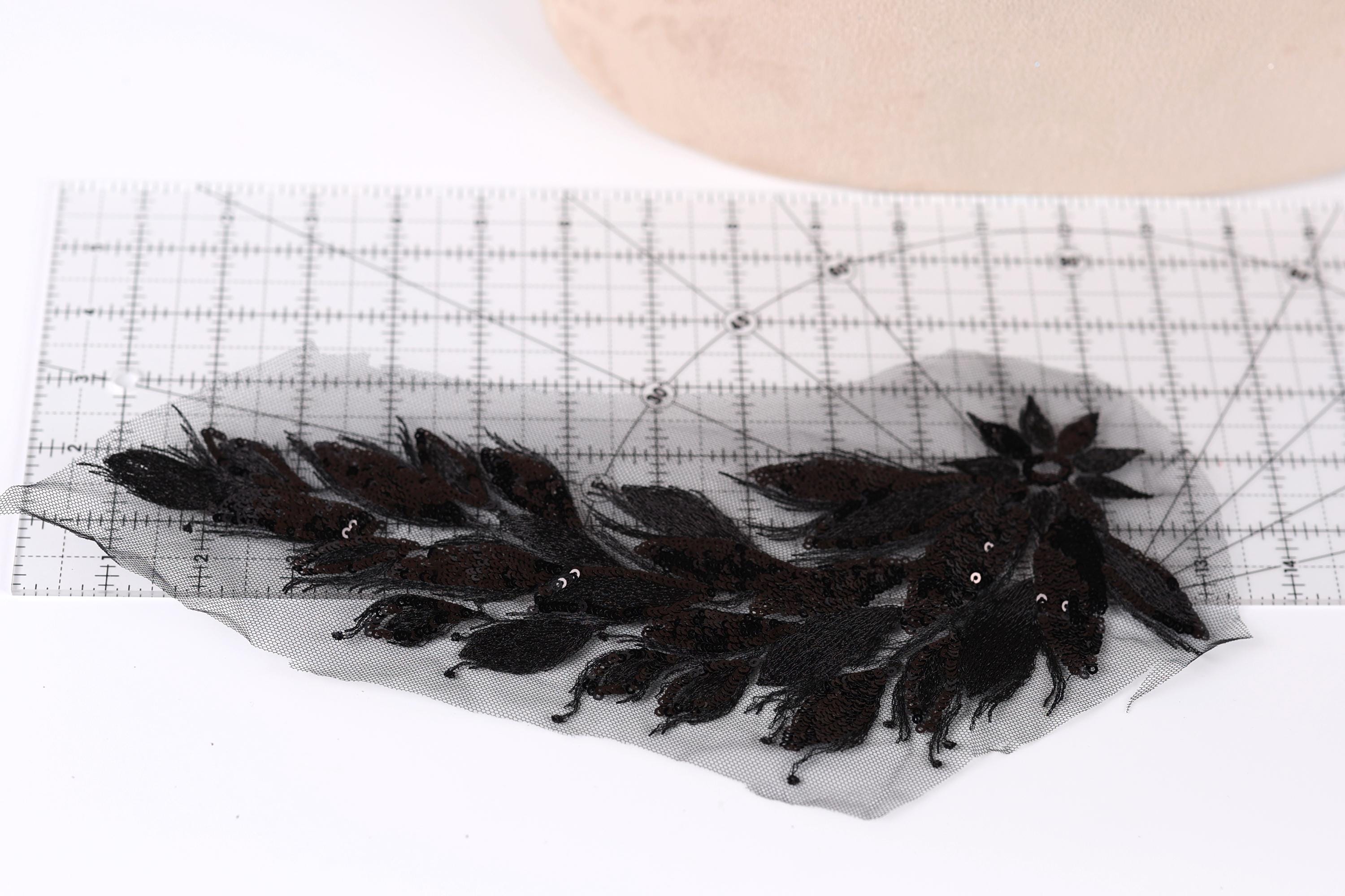 a close-up view of a black lace piece with intricate floral patterns, placed on a ruler for scale.