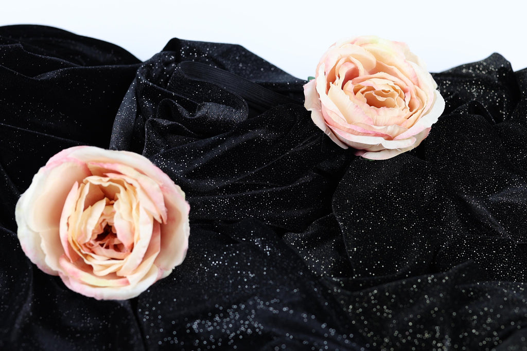 two delicate pink roses resting on a black velvet background with a sparkling effect.