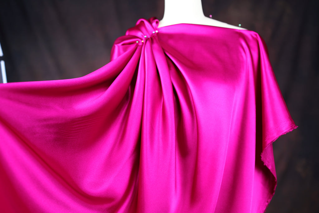 A close-up view of a vibrant pink satin fabric draped over a mannequin, showcasing its flowing and draped appearance.