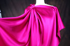 A close-up view of a vibrant pink satin fabric draped over a mannequin, showcasing its flowing and draped appearance.