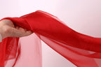 A hand is holding a red fabric, which appears to be a sheer or sheer-like material.