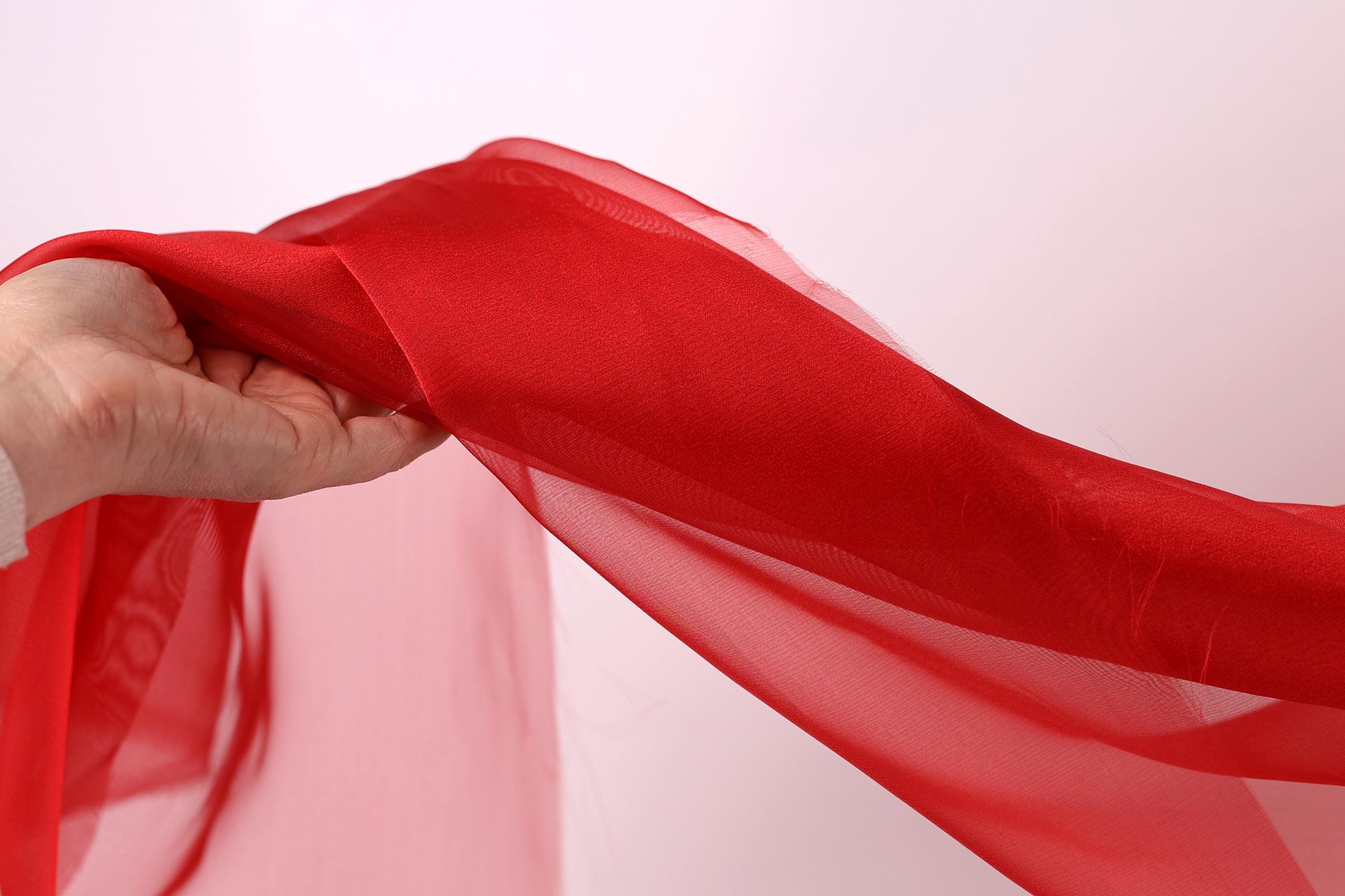 A hand is holding a red fabric, which appears to be a sheer or sheer-like material.