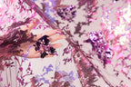 A hand is holding a piece of fabric with a floral pattern of pink and purple sequins.