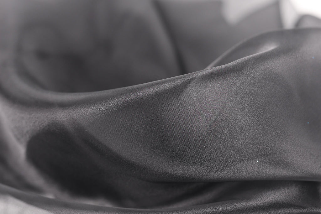 A close-up view of a soft, flowing gray fabric, possibly silk or satin, with a slightly wrinkled texture.