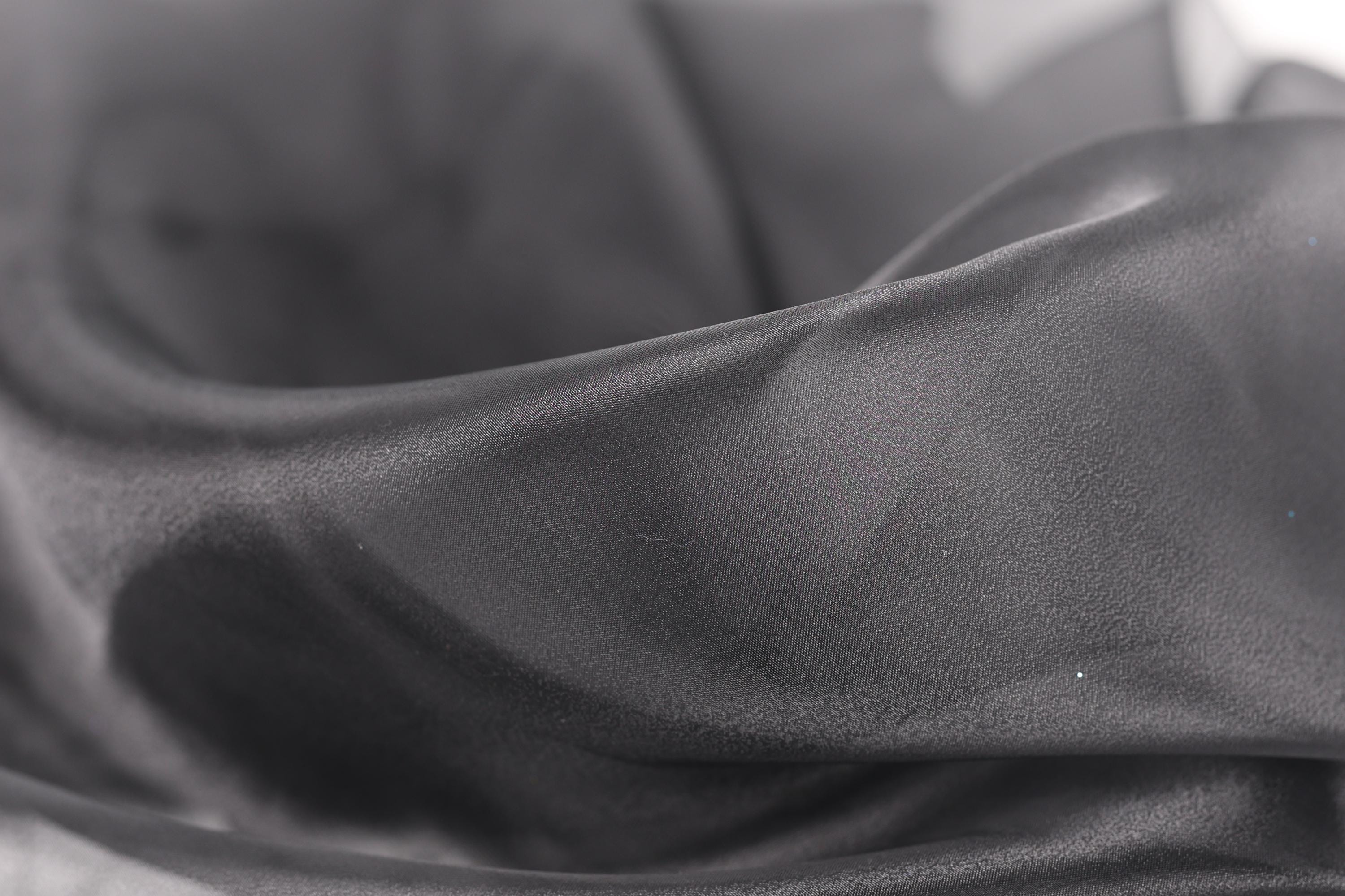 A close-up view of a soft, flowing gray fabric, possibly silk or satin, with a slightly wrinkled texture.