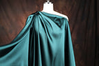 A mannequin wearing a green satin one-shoulder dress with a flowing, draped design.